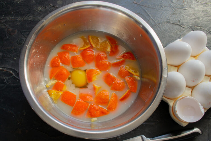 Adding eggs to the batter for the orange semolina cake. Two eggs being cracked into the bowl with the orange and whey mixture.