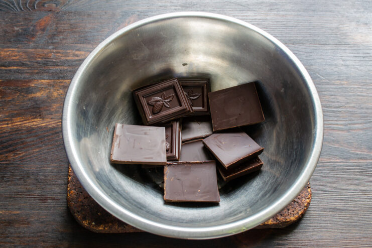 Breaking a dark chocolate bar for melting A bar of dark chocolate being broken into small pieces in a white bowl.