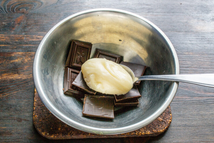 Adding honey to the dark chocolate pieces Honey being drizzled over pieces of dark chocolate in a white bowl.