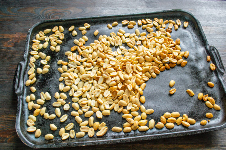 Roasting peanuts on a baking sheet until golden Blanched peanuts spread on a baking sheet, roasted to a light golden color.