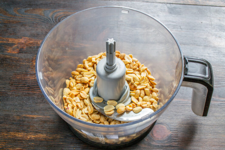 Pouring roasted peanuts into a blender Roasted peanuts being poured from a baking sheet into a blender container.