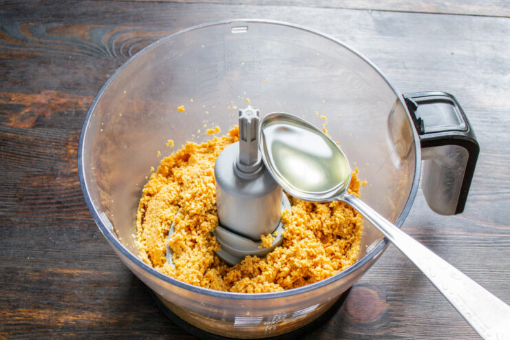 Adding neutral vegetable oil to the peanut butter Pouring a stream of clear vegetable oil into the peanut butter in a blender.