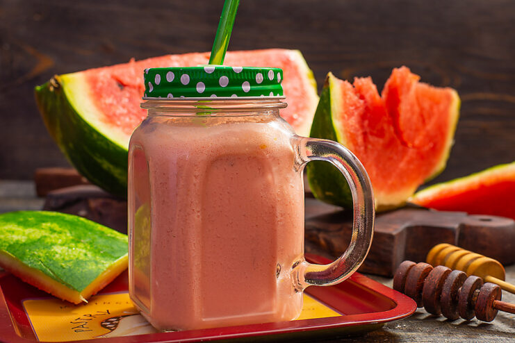 A tall glass of pink watermelon smoothie with honey, ready to drink.