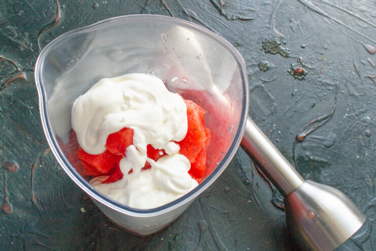 Adding Greek Yogurt for a Creamy Smoothie Spoonful of thick Greek yogurt being added to the blender with watermelon.