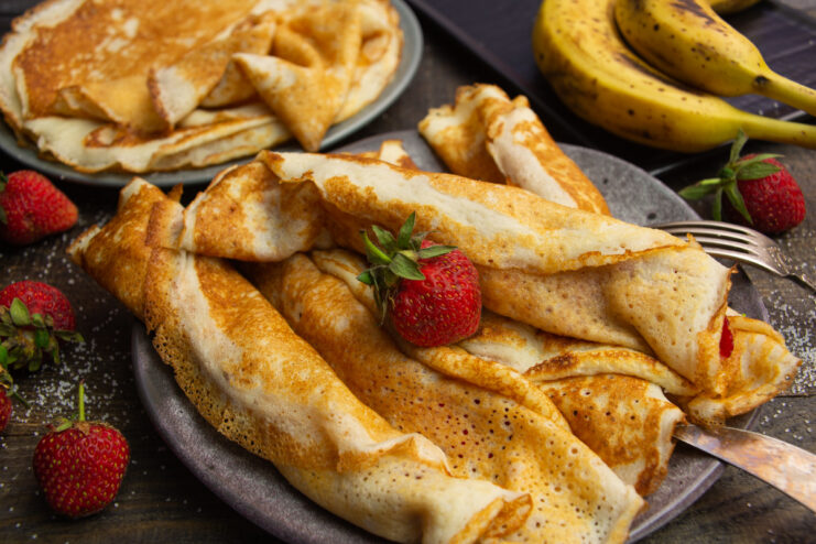 A plate of delicate lacy crepes rolled and filled with a fresh strawberry and banana fruit salad.