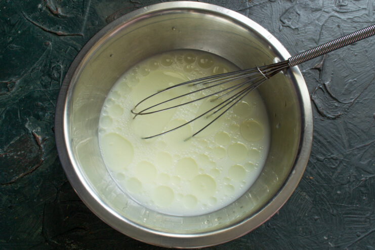 A hand pouring milk from a glass into a white bowl that already contains kefir.