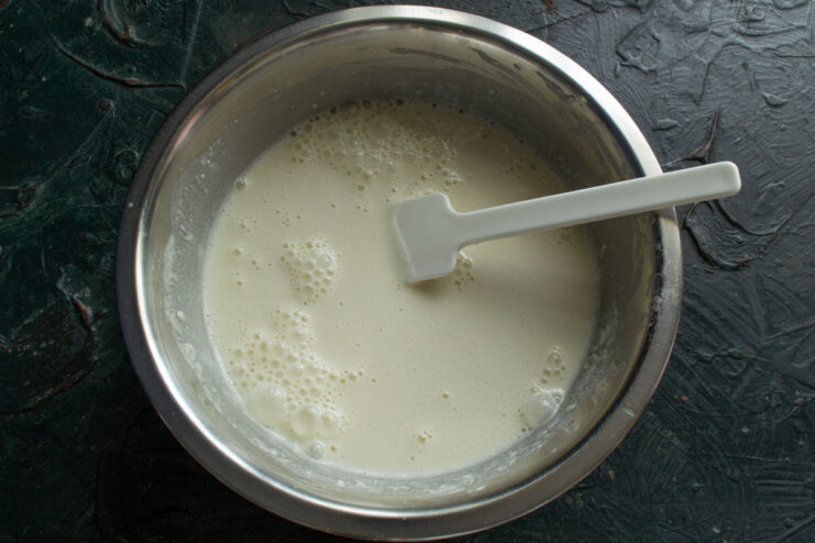 Whisking the crepe batter in a white bowl until it is smooth and free of lumps.