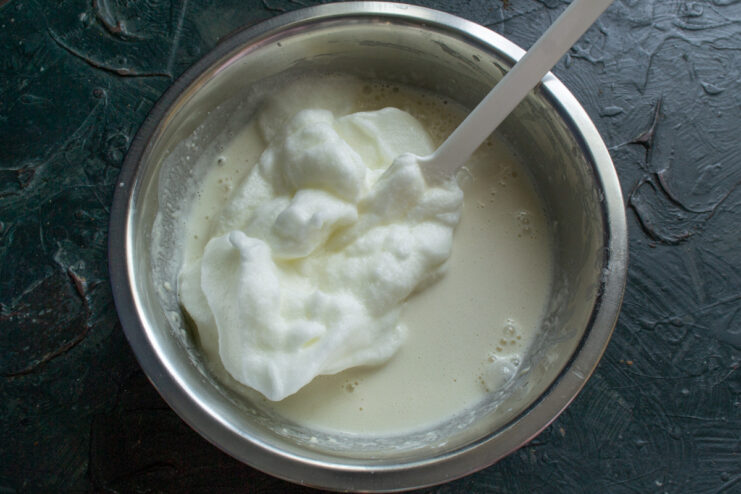 Electric mixer whipping egg whites in a glass bowl until they form stiff, glossy peaks.