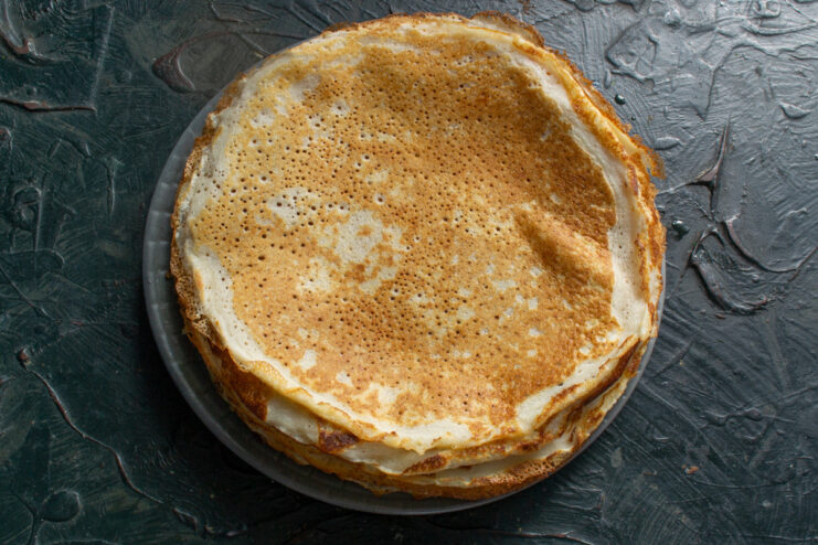A tall, neat stack of freshly cooked, golden-brown lacy crepes on a plate.