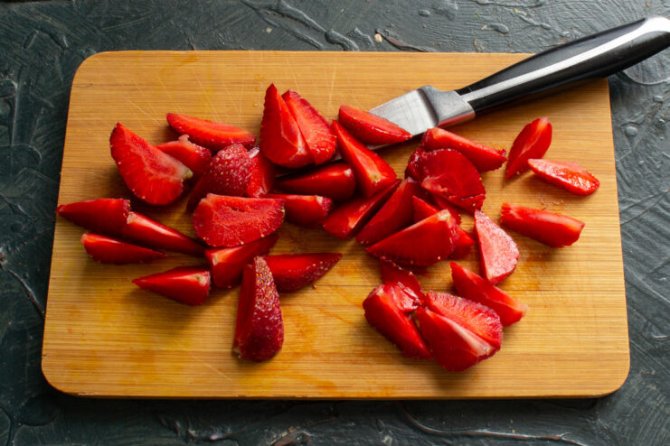 A close-up of fresh, ripe strawberries being sliced into small pieces on a cutting board.