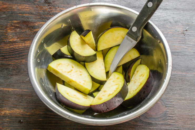 Step 1: How to Properly Slice Eggplant for Frying An eggplant being sliced into half-moon shapes on a wooden cutting board.