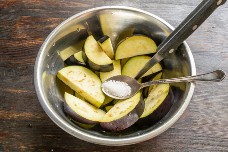 Salting Eggplant to Draw Out Moisture and Bitterness Sliced eggplant in a bowl, sprinkled with salt to prepare for cooking.