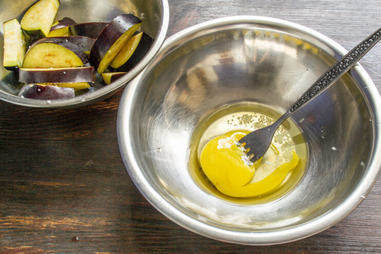 Preparing the Egg Wash for Breading A raw egg cracked into a white bowl with a pinch of salt, ready to be whisked.