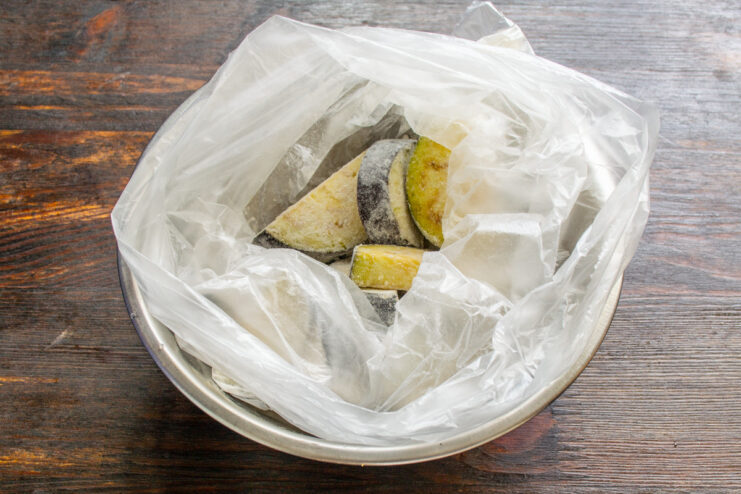 Easy Way to Coat Eggplant in Flour Using a Bag Sliced eggplant being shaken in a plastic bag with flour for an even coating.