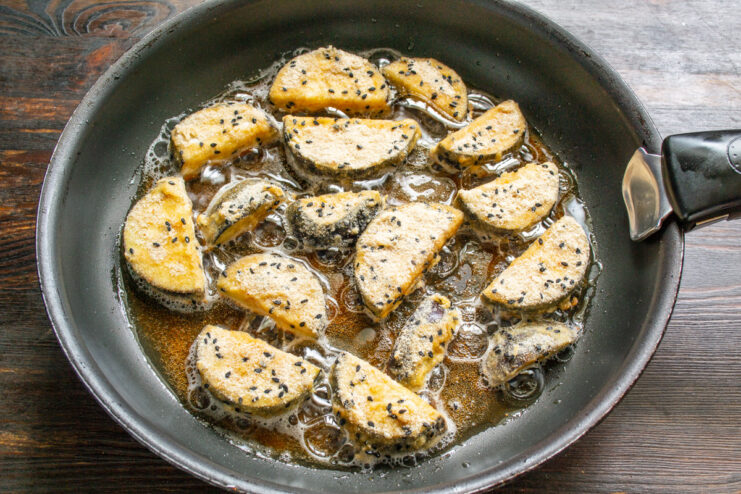 Frying the Breaded Eggplant to Golden Perfection Breaded eggplant pieces being placed into a frying pan with hot oil.