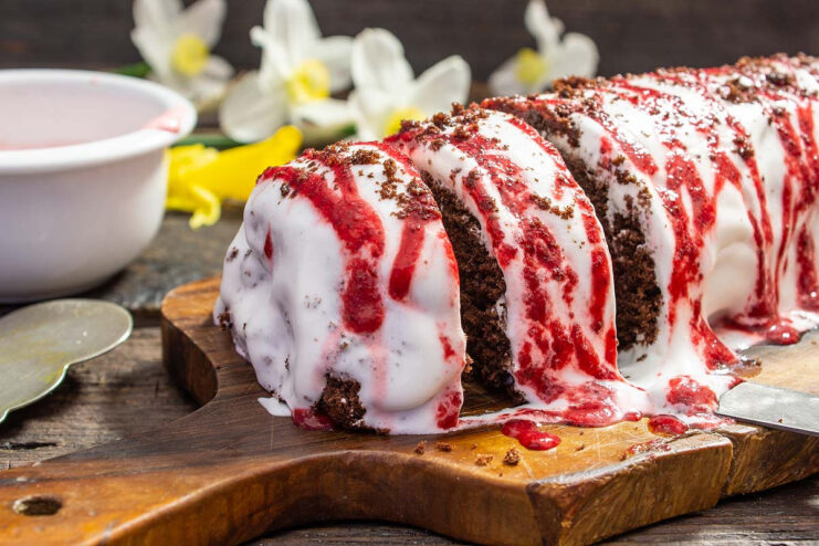 A finished gluten-free chocolate strawberry sponge roll on a plate, decorated with cream and strawberries.