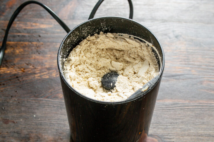 How to make homemade oat flour for your gluten-free baking. A bowl of oat flour next to a coffee grinder filled with rolled oats.