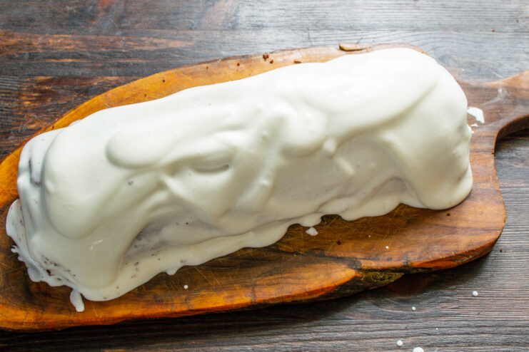 Covering the entire sponge roll with a generous layer of cream. The chocolate sponge roll completely covered in white smetana cream.
