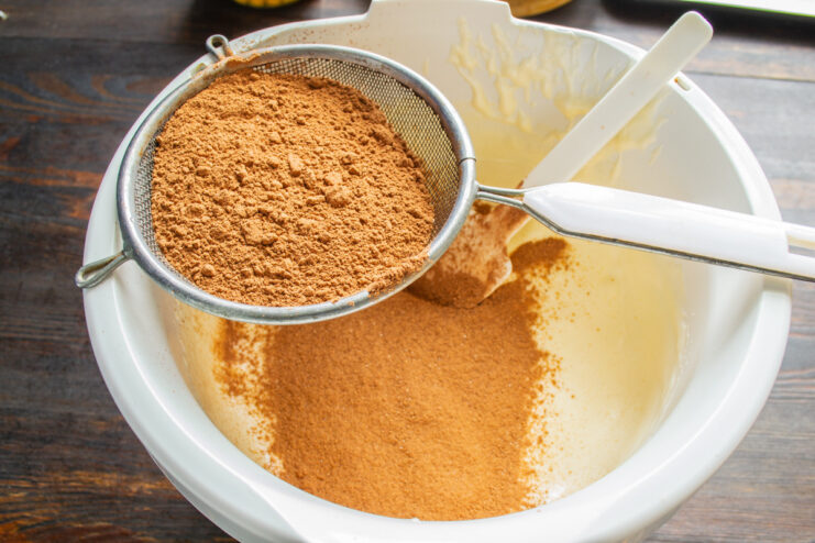 Gently folding in the dry ingredients to keep the batter airy. Sifting the cocoa and oat flour mixture into the whipped egg batter.