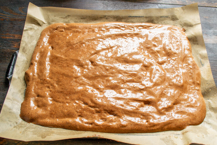 Spreading the sponge cake batter evenly on a baking sheet. Chocolate sponge cake batter spread evenly on a baking sheet lined with parchment paper.