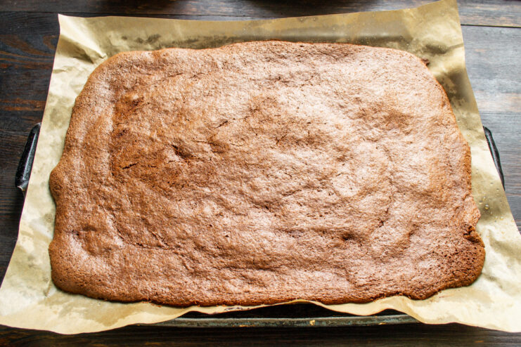 The thin sponge cake bakes quickly in a preheated oven. The baking sheet with the chocolate sponge cake inside an oven.
