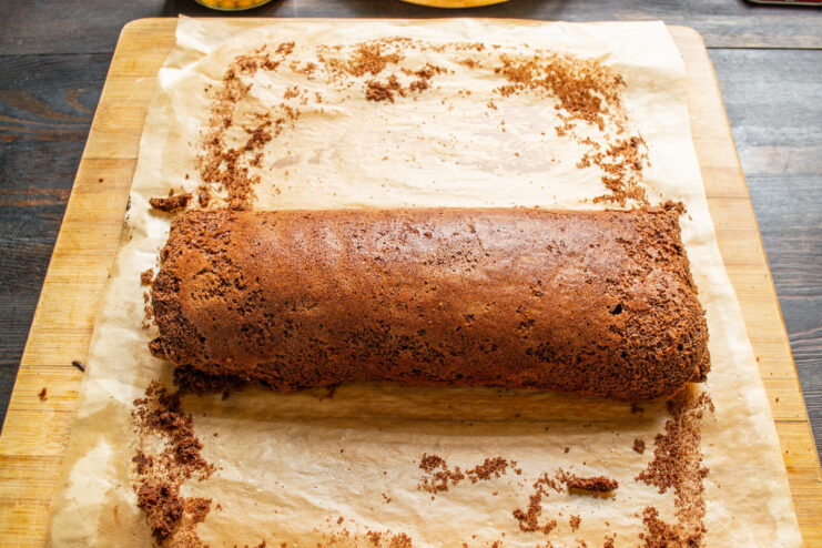 Rolling the hot sponge cake immediately prevents it from cracking. A hot, freshly baked chocolate sponge cake being rolled up in its parchment paper.