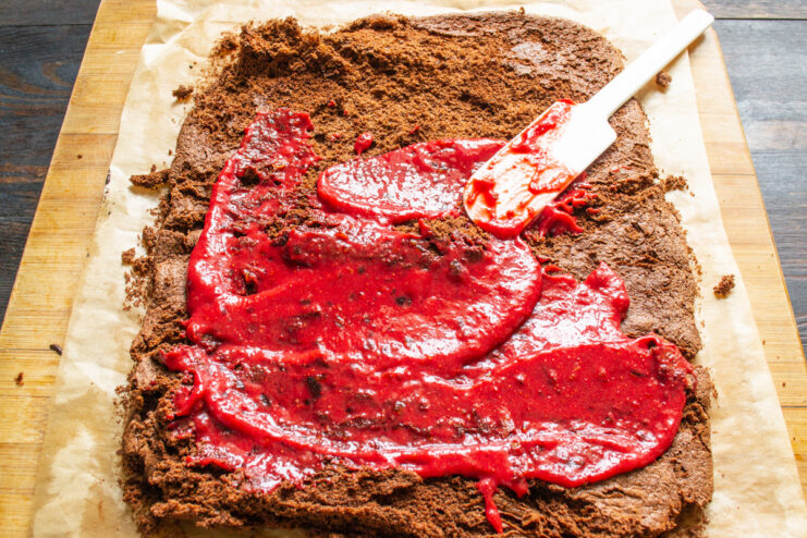 Spreading the delicious and healthy strawberry-date filling. The unrolled chocolate sponge cake being covered with a layer of pink strawberry filling.