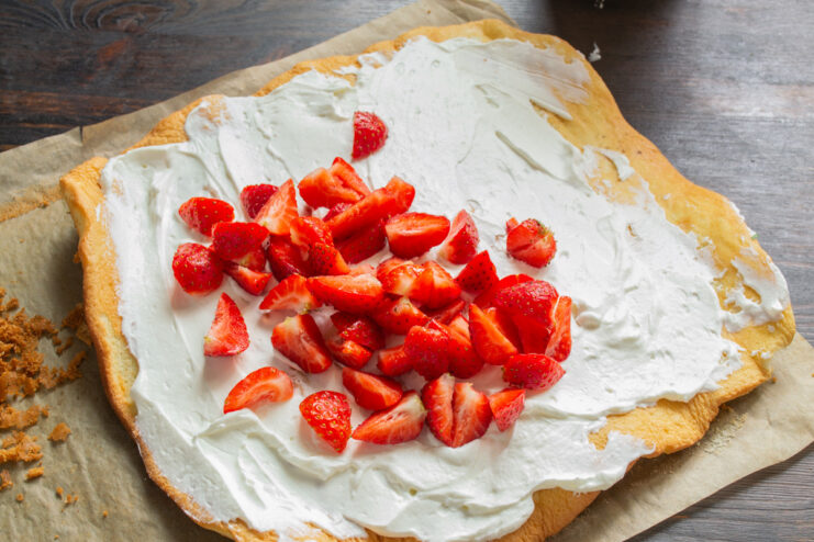 Adding Fresh Strawberries to the Cream Filling Chopped fresh strawberries being scattered over the whipped cream filling on the sponge cake.