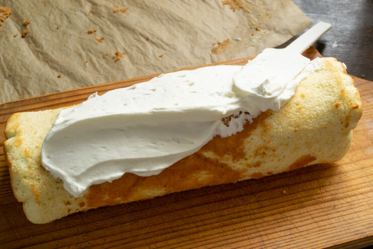 Frosting the Outside of the Sponge Roll with Whipped Cream A finished sponge roll being frosted on the outside with the remaining whipped cream.