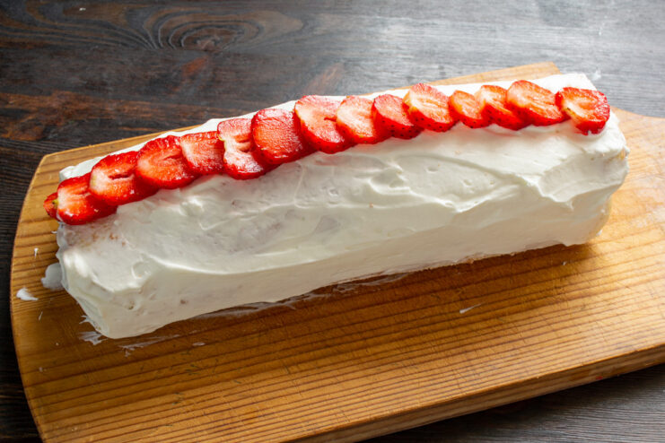 Decorating the Sponge Roll with Fresh Strawberry Slices Decorating the top of the cream-frosted sponge roll with slices of fresh strawberries.