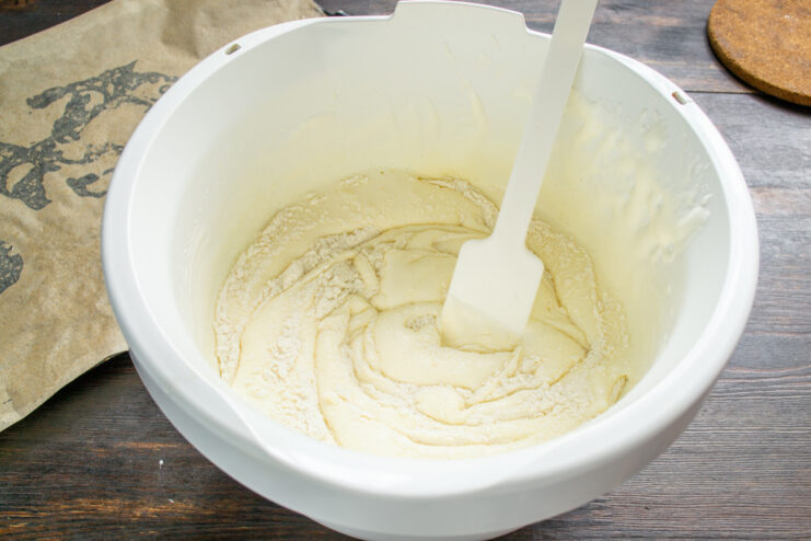 Folding Flour into the Egg Mixture for a Light Sponge Folding flour into the whipped egg batter in a glass bowl with a spatula.