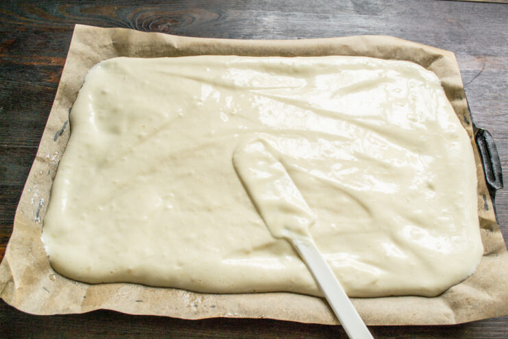 Spreading the Sponge Batter Evenly on the Baking Tray Sponge roll batter being spread evenly on a parchment-lined baking tray with a spatula.