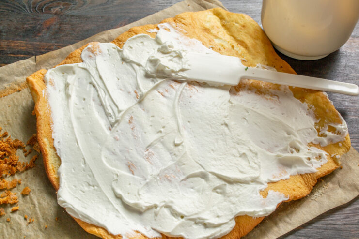 Spreading Whipped Cream Filling on the Sponge Cake Spreading a layer of whipped cream over the unrolled sponge cake with a spatula.