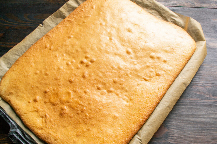 Removing the Golden-Brown Sponge Cake from the Oven A perfectly baked golden-brown sponge cake on a baking sheet just out of the oven.