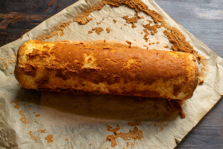 Rolling the Hot Sponge Cake into a Log A hot sponge cake being carefully rolled up with parchment paper to set its shape.