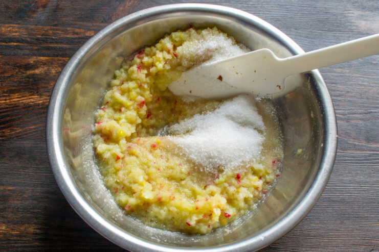 Adding Sugar to the Fruit Puree Adding granulated sugar to the bowl of apple and lemon puree for the filling.