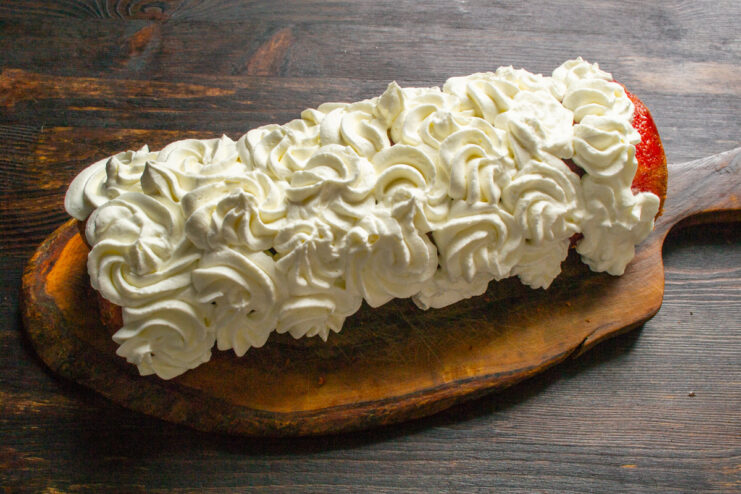 Decorating the Sponge Roll with Whipped Cream Piping whipped cream decoratively on top of the finished lemon and apple sponge roll.