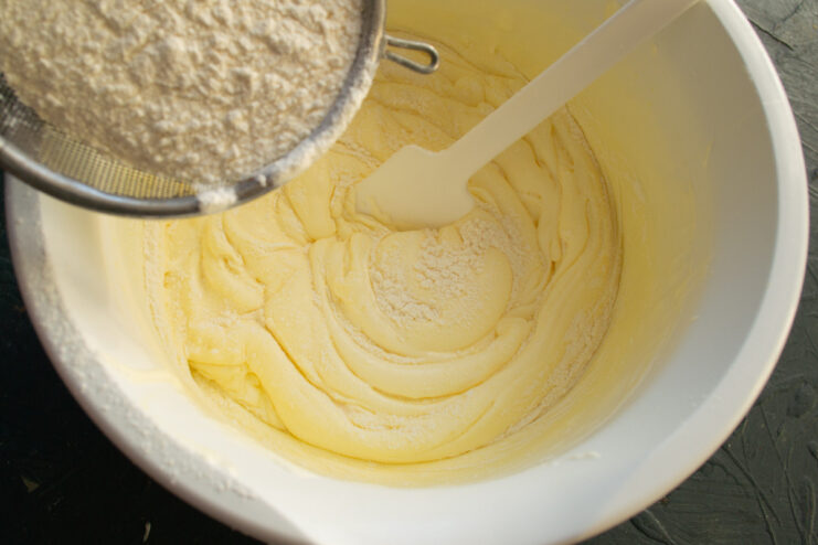 Whipping Eggs and Sugar for a Fluffy Sponge Base A mixer whipping eggs and powdered sugar in a glass bowl until pale and thick.