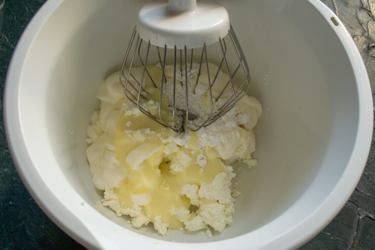 Adding Condensed Milk to the Cream Mixture Pouring cold condensed milk into the bowl with the cottage cheese cream mixture.