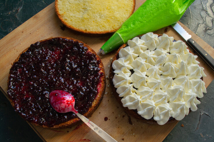 Piping the Cream onto the Jam-Covered Layers Piping cottage cheese cream from a piping bag onto a cake layer spread with jam.