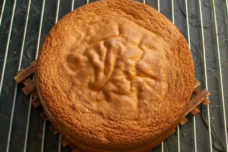 Cooling the Freshly Baked Sponge Cake A golden-brown baked sponge cake cooling on a black metal wire rack.