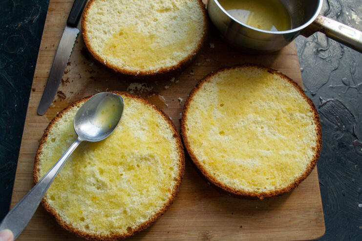 Soaking the Cake Layers with Flavorful Orange Syrup Brushing a layer of sponge cake with orange syrup to add moisture and flavor.