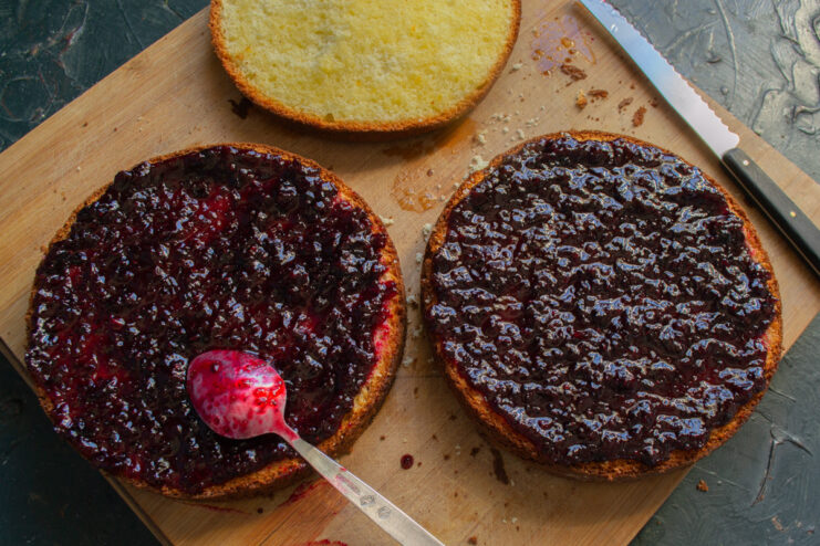 Spreading Blackcurrant Jam on the Cake Layers Spreading a layer of dark blackcurrant jam over a sponge cake layer.