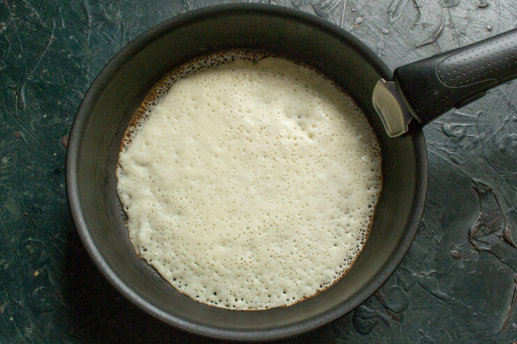 Flipping the Blinchik in the Pan A thin blinchik being cooked in a hot pan, ready to be flipped.