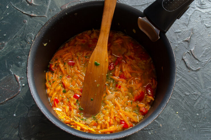 Adding chicken broth to create the sauce base Pouring chicken broth into a pan with sautéed vegetables.