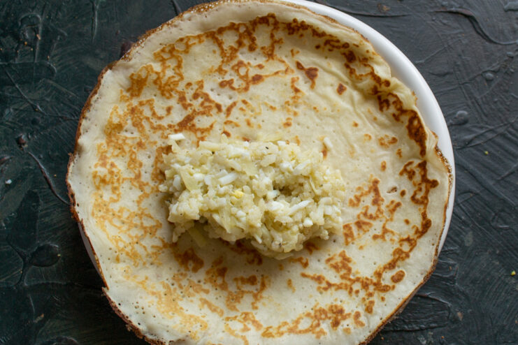 Step-by-step: How to fill the blinchiki A thin crepe laid flat with a spoonful of egg and rice filling in the center.