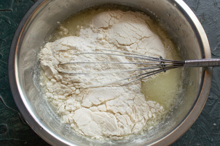 Step 2: Combining wet and dry ingredients for a smooth batter Adding flour to a bowl of wet ingredients to make crepe batter.