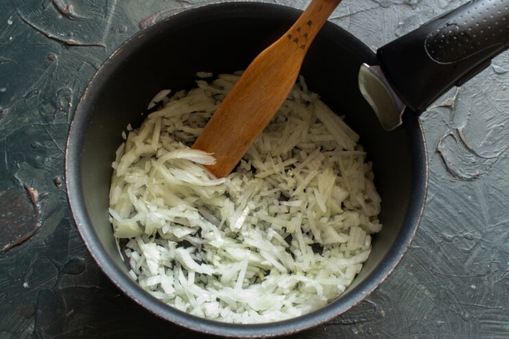 Preparing the filling: Sautéing onions until translucent Finely chopped onions being sautéed in a pan until golden.