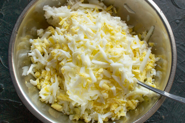 Making the filling: Combining rice and chopped eggs A bowl of cooked rice with chopped hard-boiled eggs being added.