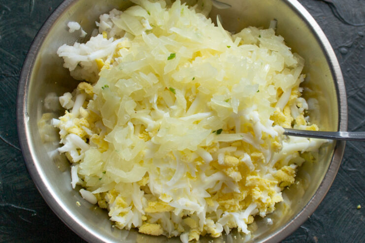 Completing the filling with flavorful sautéed onions Sautéed onions being added to the rice and egg mixture for the filling.